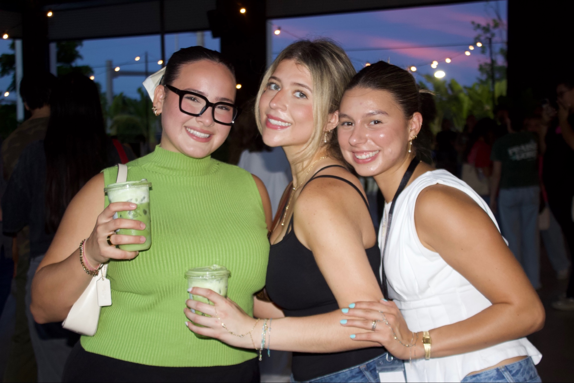 Three friends smiling together with green drinks at the market